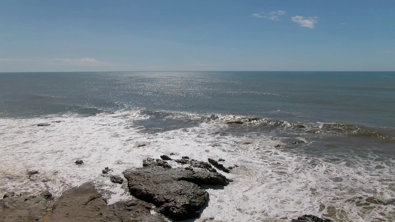 At Buzzards Beach in East Cape BCS Mexico, white waves break over dark foreground rocks under a clear blue sky with no visible people.