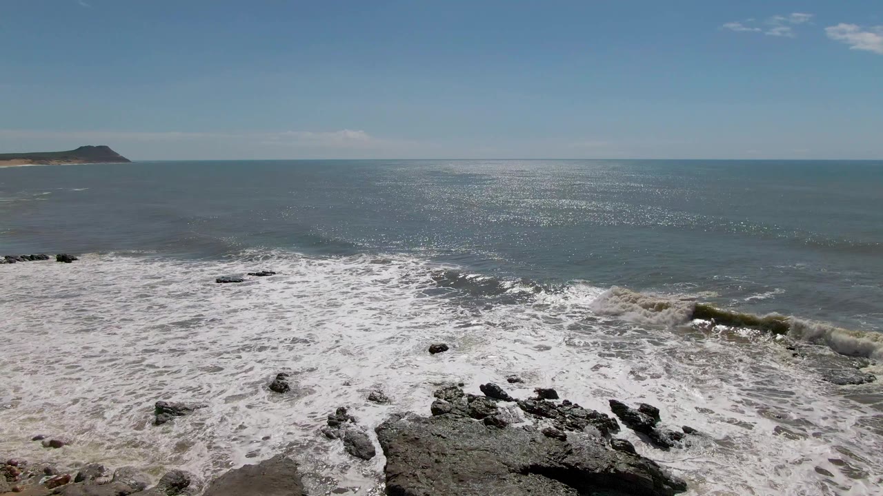 Open ocean, rocky surf, and headland at left horizon