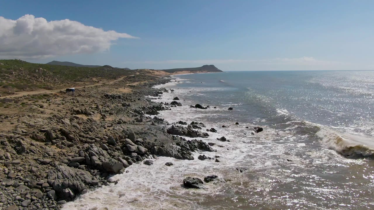Surf rolls toward rocks along an empty coastal stretch.