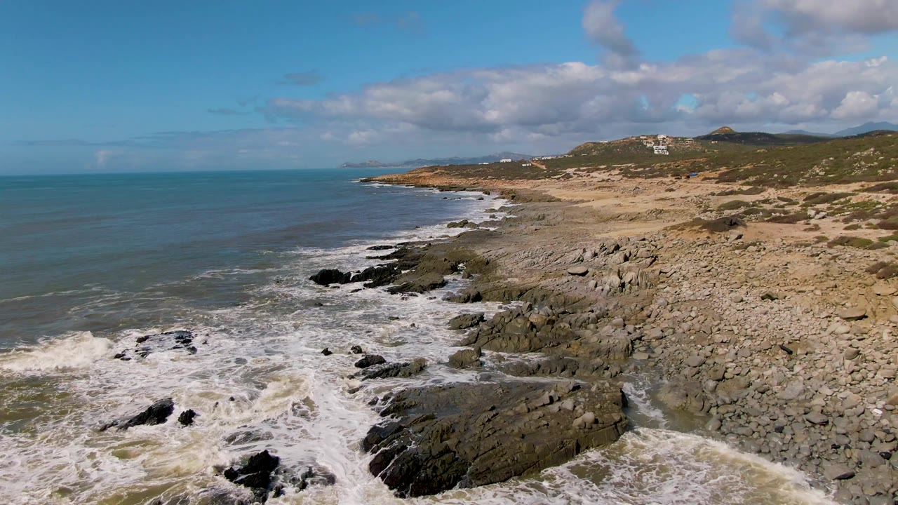 Surf rolls across black rocks on a sandy coastal stretch.