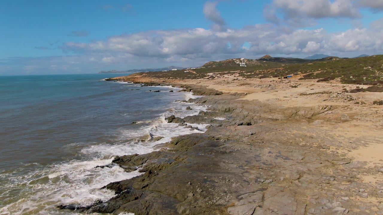 Wide aerial view of ocean surf meeting a rocky and sandy shore.