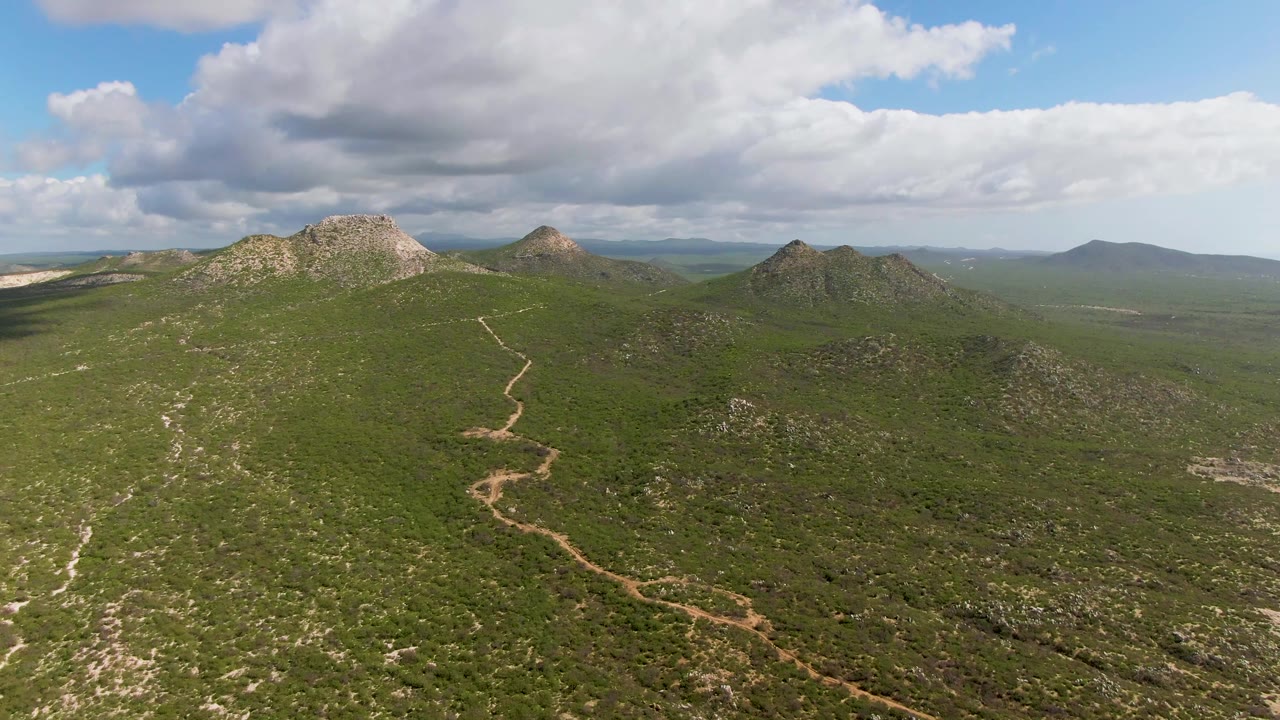 Aerial view across green hills with a rocky ridge and broad cloud bank.