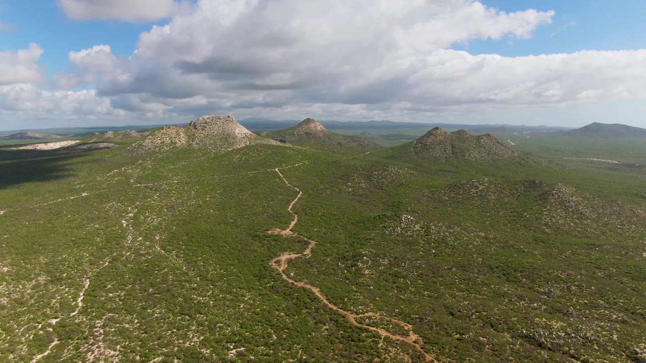 Aerial view across green brush and rocky ridges in Buzzards Beach East Cape BCS Mexico, with darker cloud shadow spreading over the left side and no visible people.