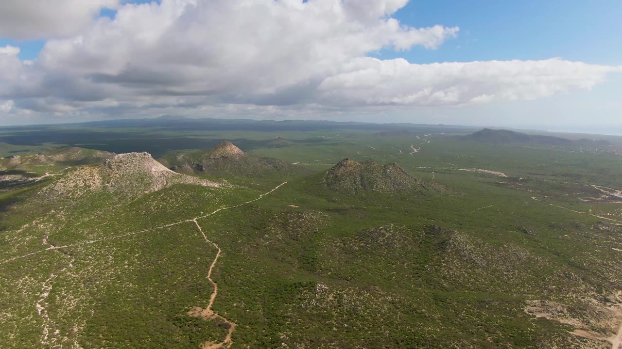 Aerial view of rocky green hills and winding tracks beneath heavy clouds.