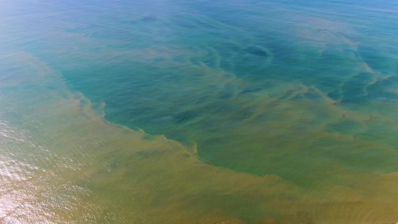Blue-green ocean surface at Buzzards Beach East Cape BCS Mexico with pale shifting water patterns, sun glare near the lower left, and no visible people.