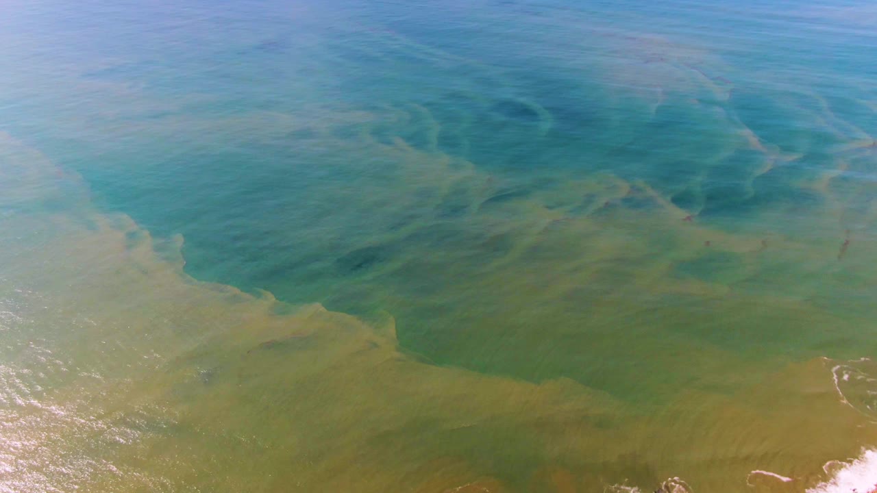 Turquoise and green ocean surface with shallow wave foam near the lower right