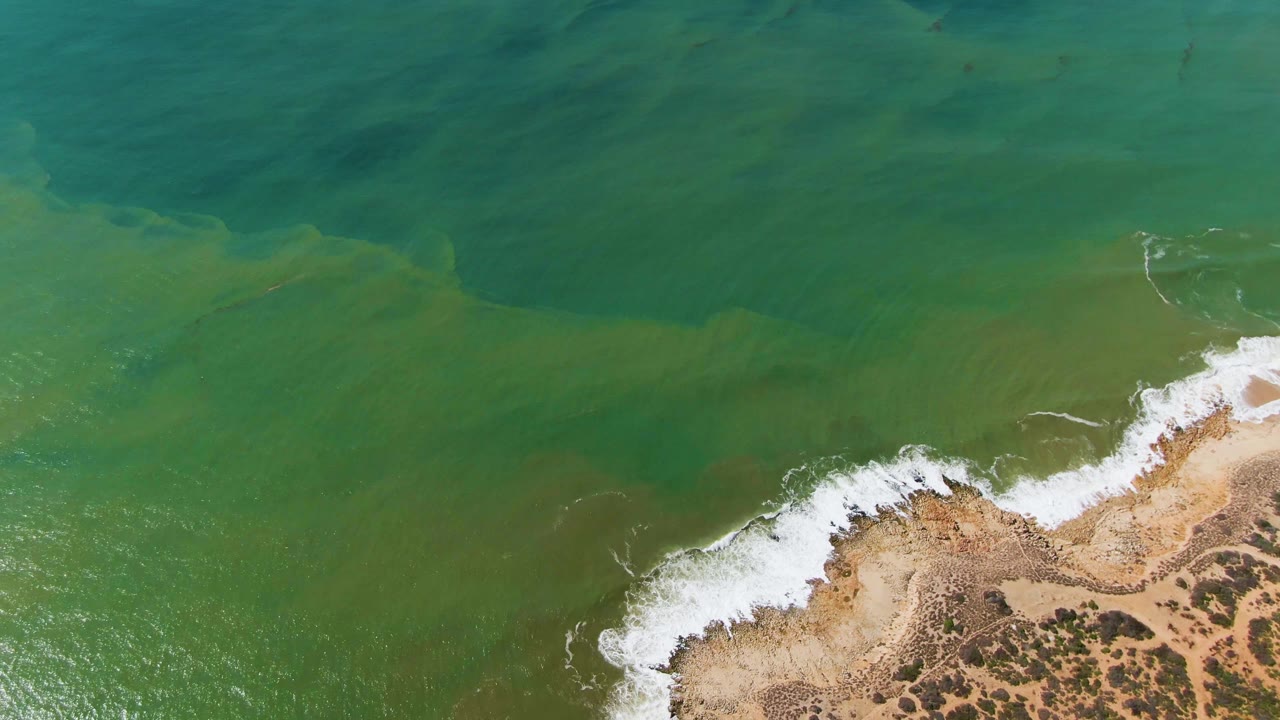 Aerial frame over Buzzards Beach East Cape BCS Mexico with a larger white wave line curling onto the sandy rocky coast and no visible people.