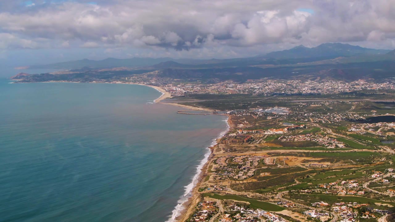 Coastal aerial with ocean foreground, surf, developed shore, and mountain horizon