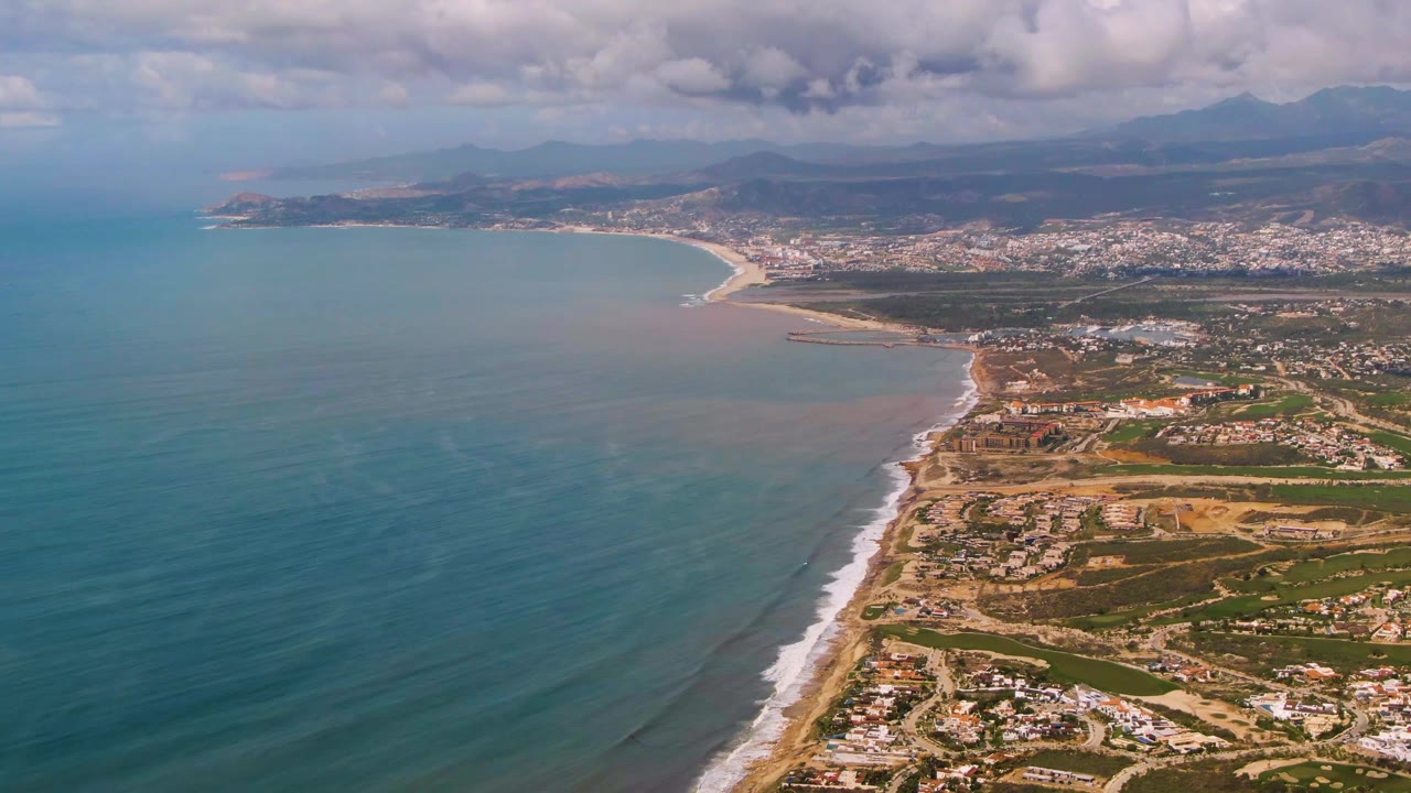 Wide drone view of ocean and beach beside a coastal town.