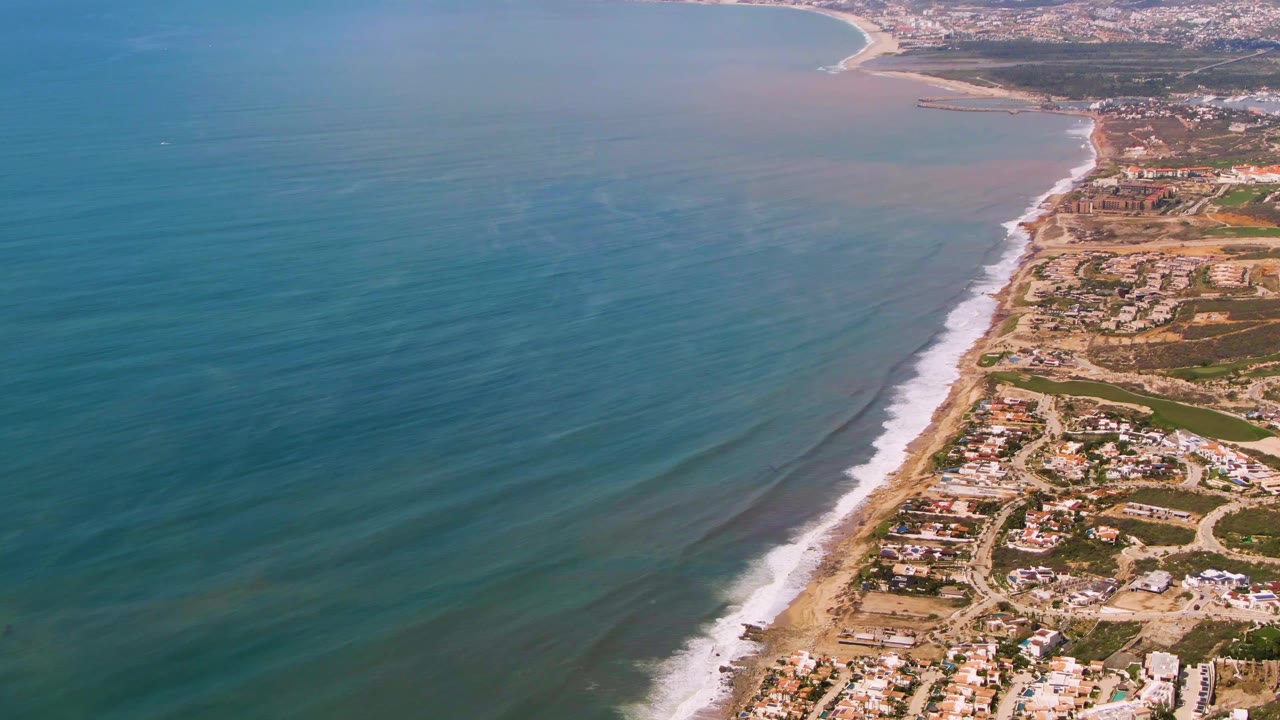 Aerial coastal neighborhood beside a long sandy beach and calm water.