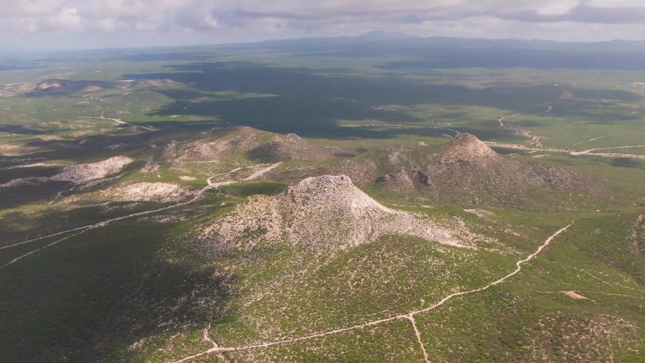 Aerial landscape with rocky hills, green valley, cloud shadows, and distant mountains.