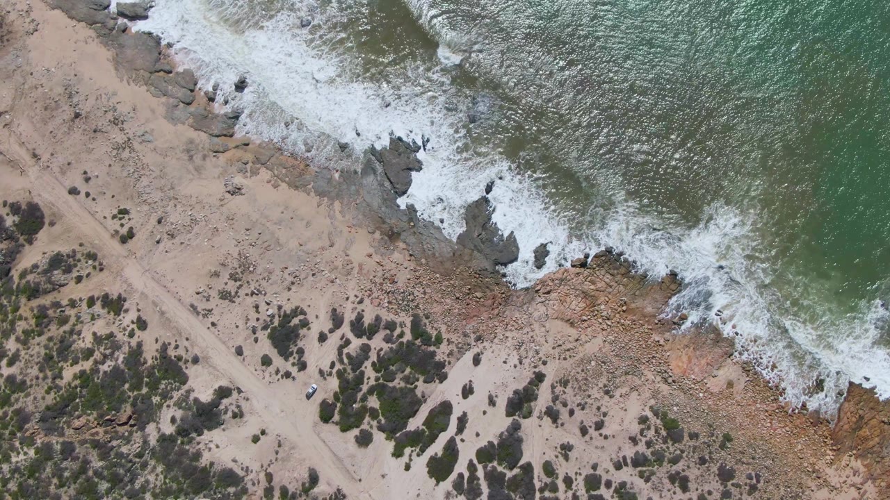 Surf washing across rocks near a sandy beach path