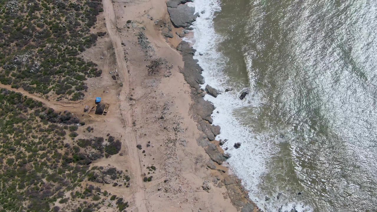 Rocky coast and dirt path seen from above as waves break