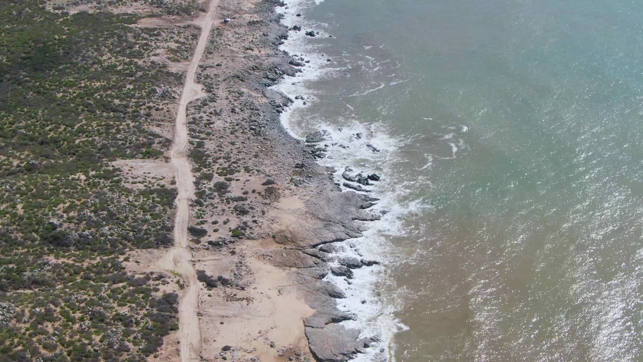 Top-down coast view with dirt road, scrub, rocks, and ocean