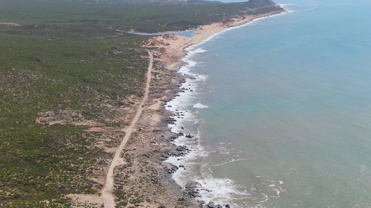 High coastal view with road parallel to surf and hills beyond.