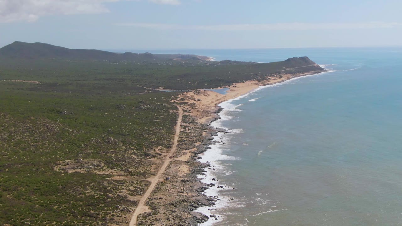 Aerial view of a dirt road beside a sandy beach and ocean waves.