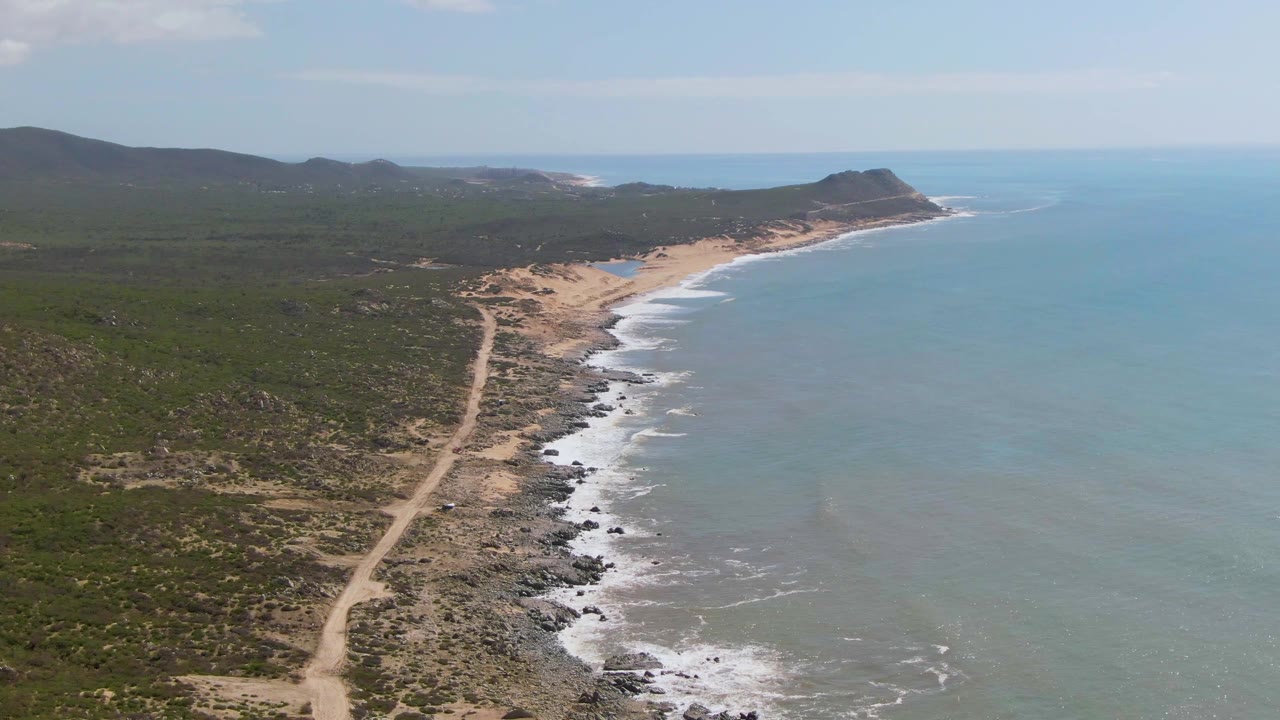 Wide aerial shoreline with dirt road and surf beside open water