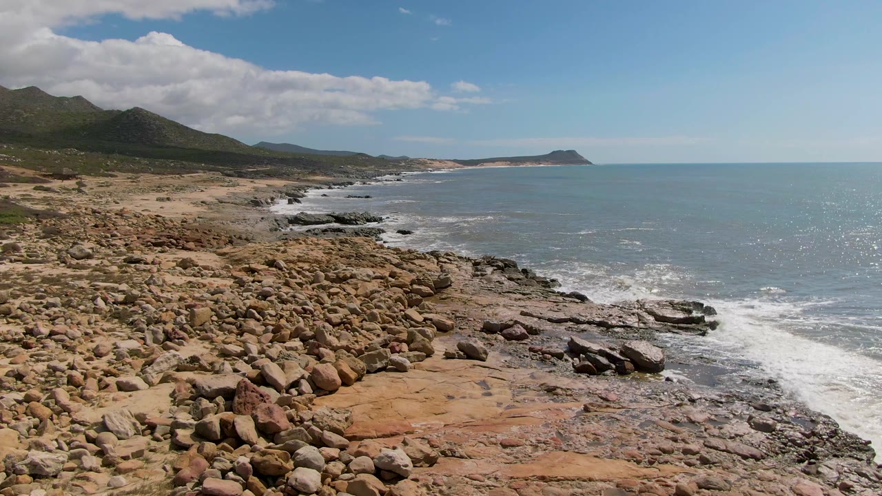 Boulder-covered coast beside blue ocean under clouds.