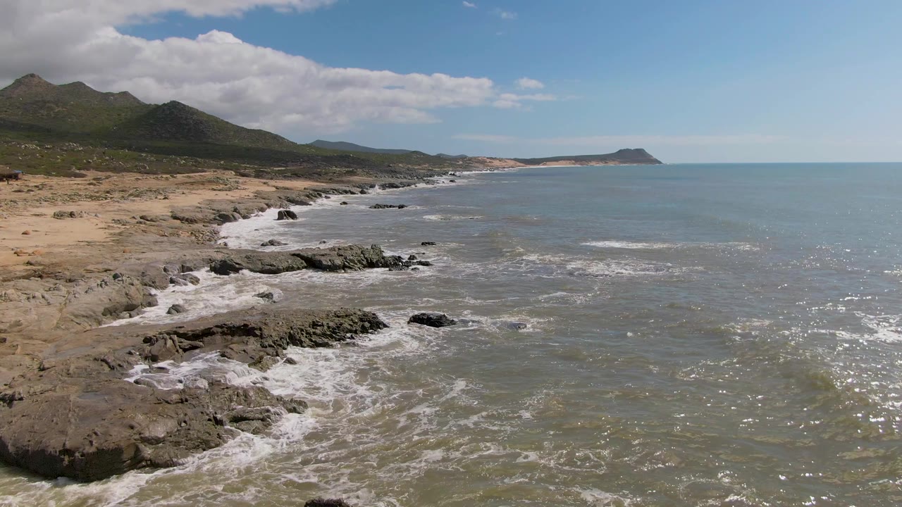 Rocky shoreline with waves, sandy coast, mountains, and ocean