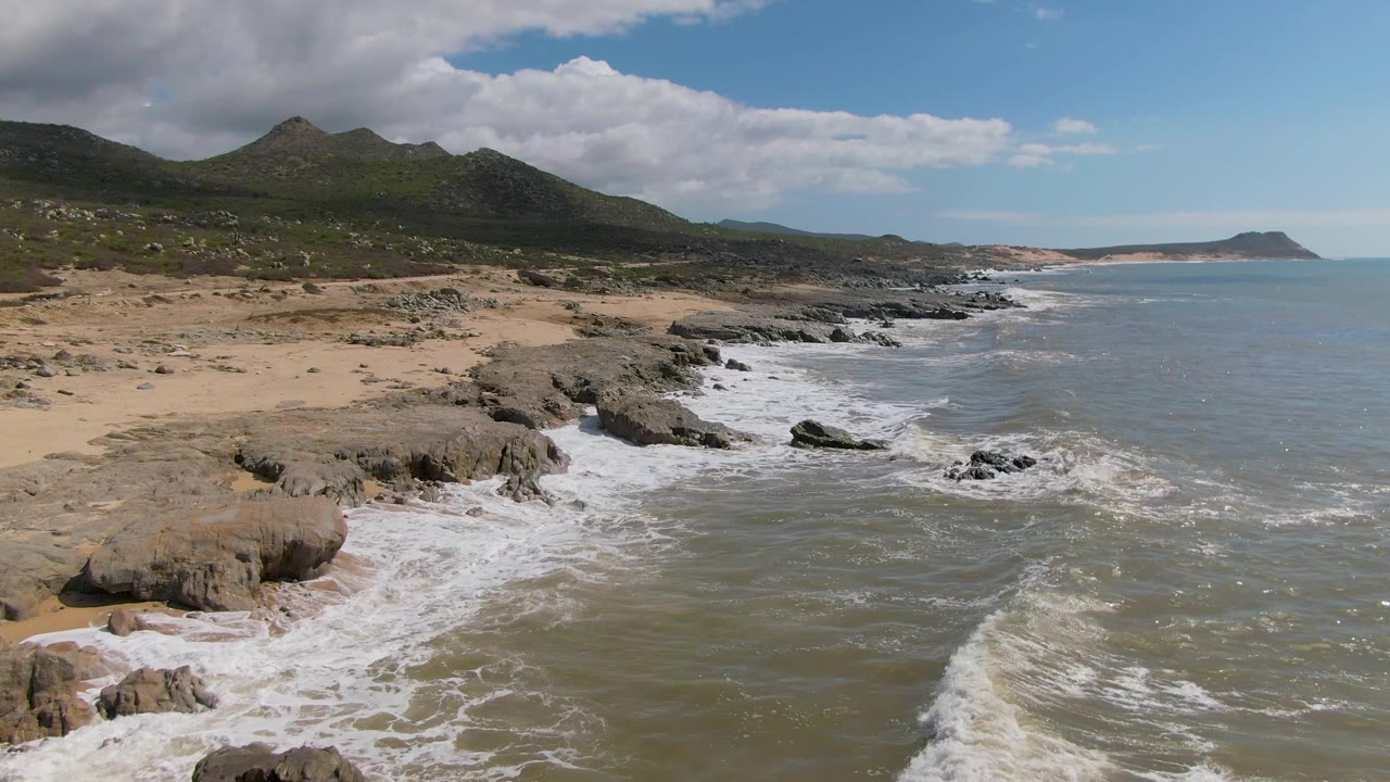 Wide aerial coastline with waves washing over rocks and sand
