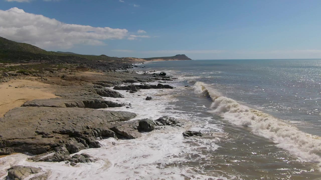 Rocky shoreline with surf breaking beside a sandy beach