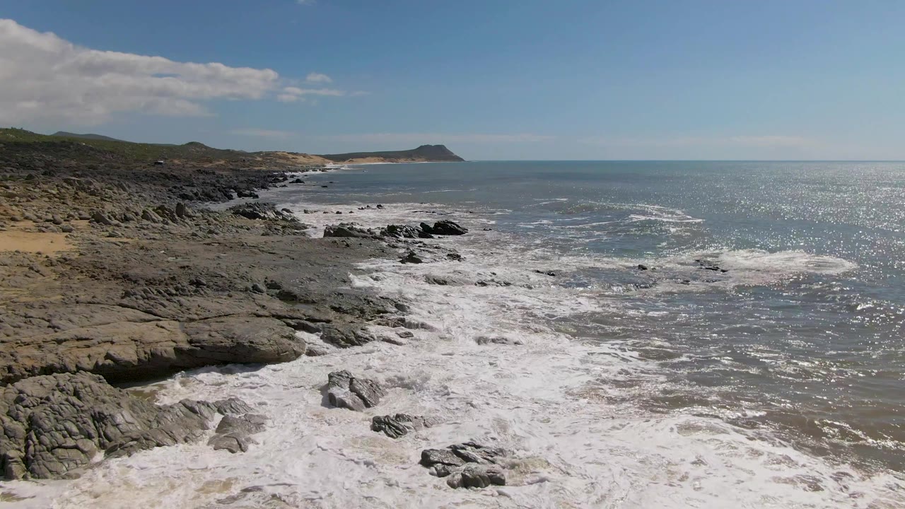 Rocky shoreline and foamy waves with distant headland.