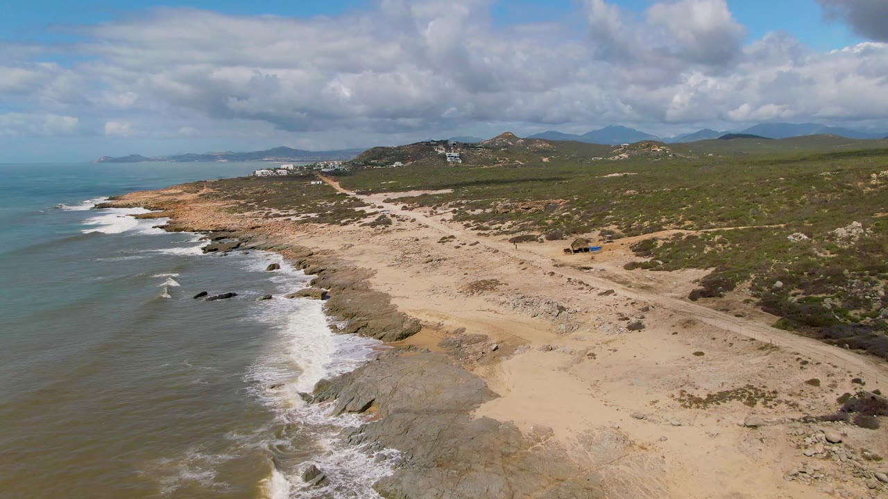 Aerial shot of beach road and rocky surf with a small vehicle near the shore.