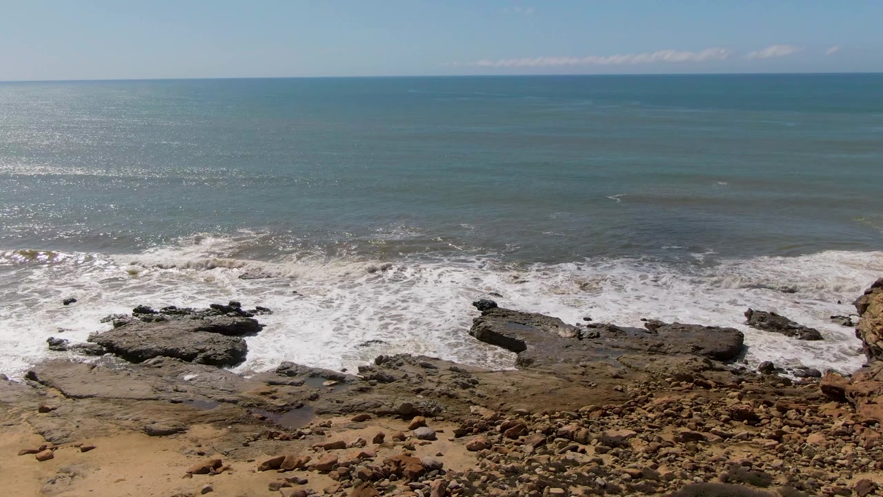Rocky shoreline with waves breaking under blue ocean horizon.