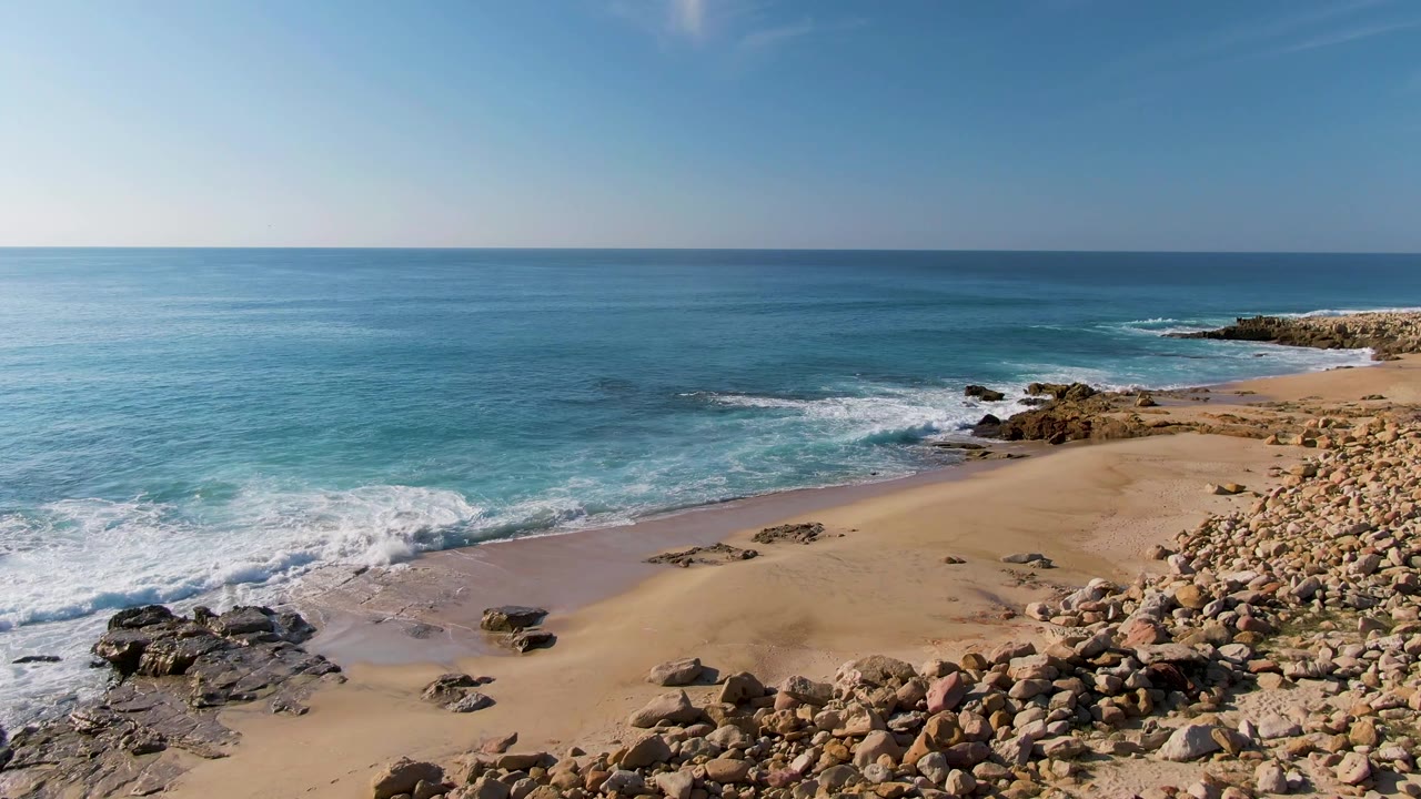 Waves wash across a sandy beach with rocks along the right foreground.