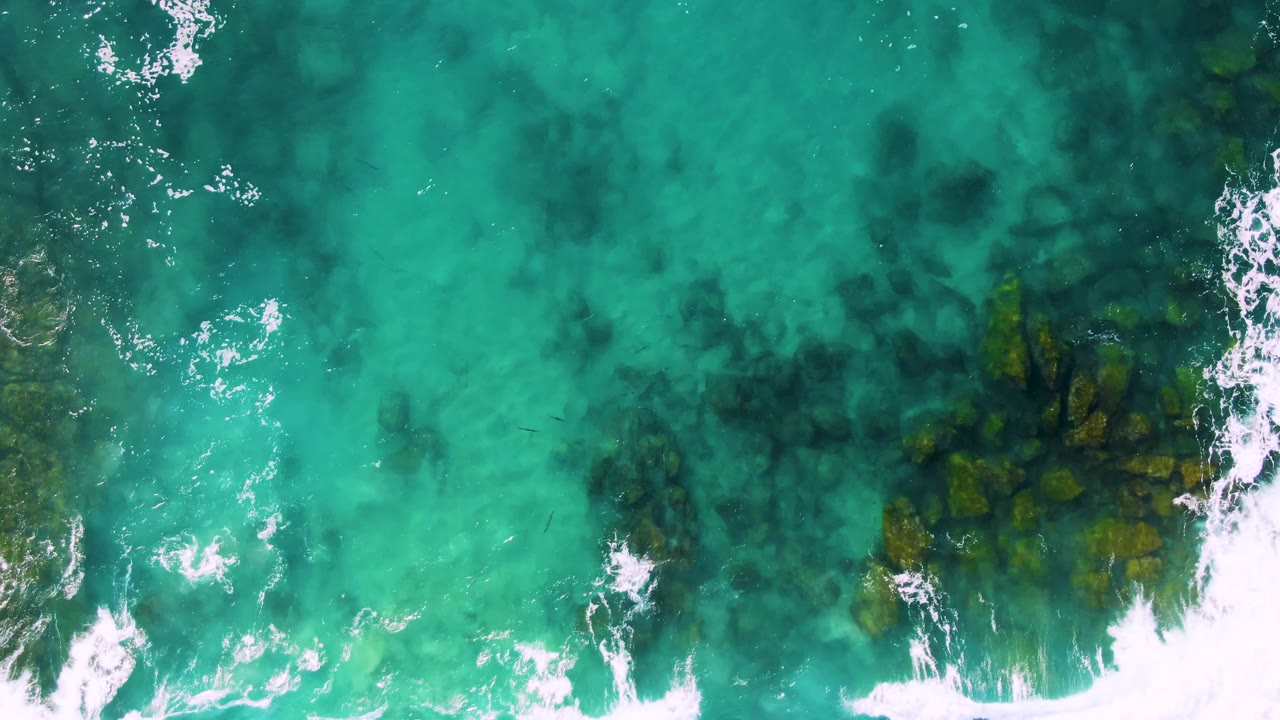 Turquoise ocean water over dark underwater rocks with white foam.