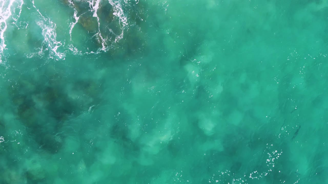 Clear green-blue water with foam crossing submerged rocks.
