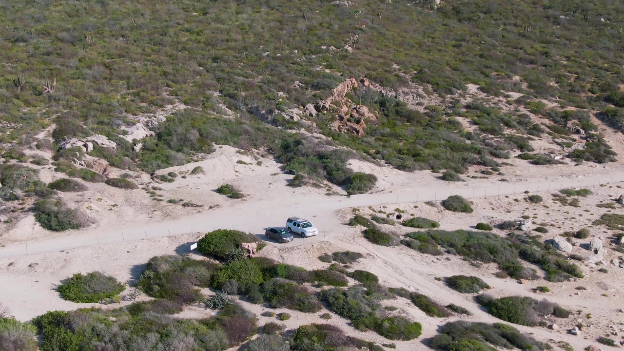 White SUV crossing a sandy trail below scattered shrubs and rocks.