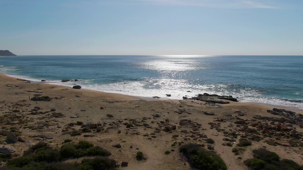 Aerial view of sandy beach, rocky shore, waves, and sunlit ocean