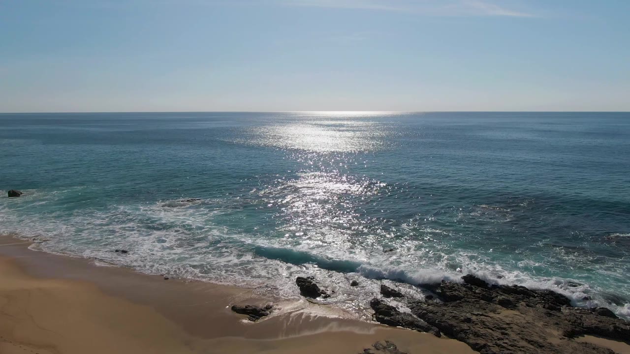 Rocky shoreline with foamy waves and bright sun reflection on the sea.