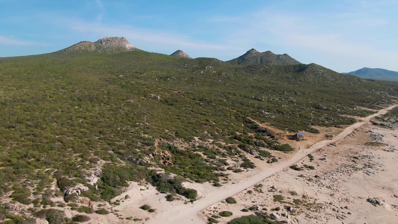 Buzzards Beach East Cape BCS Mexico aerial frame with the pale road crossing the lower landscape, a small car near the road, scrub vegetation, rocky ridges, and no visible people.