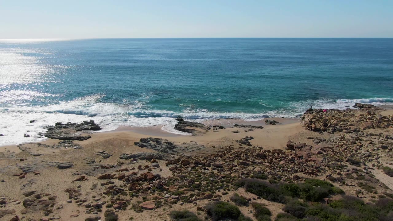 Wide aerial beach frame with waves and rocky outcrops