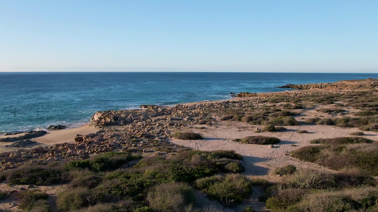 Second frame shows the Mexico shoreline from an elevated angle, with a sandy path through scrub, tan rocks near the beach, small surf, and no visible people.