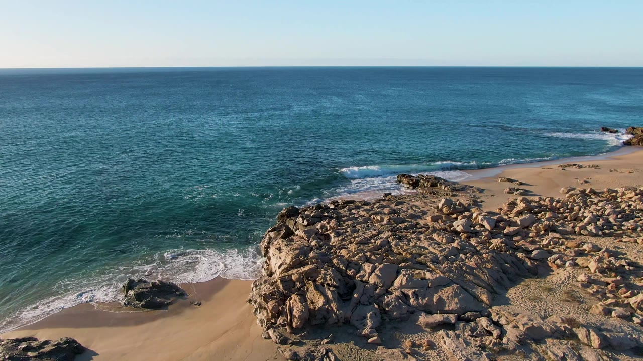 Ocean waves break beside a rocky outcrop and sandy beach.