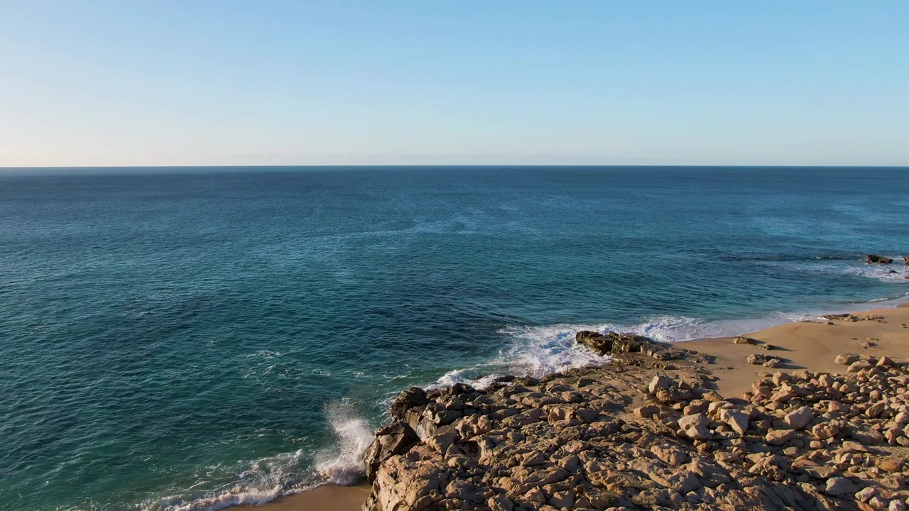 Elevated view of waves breaking against rocks beside a sandy beach