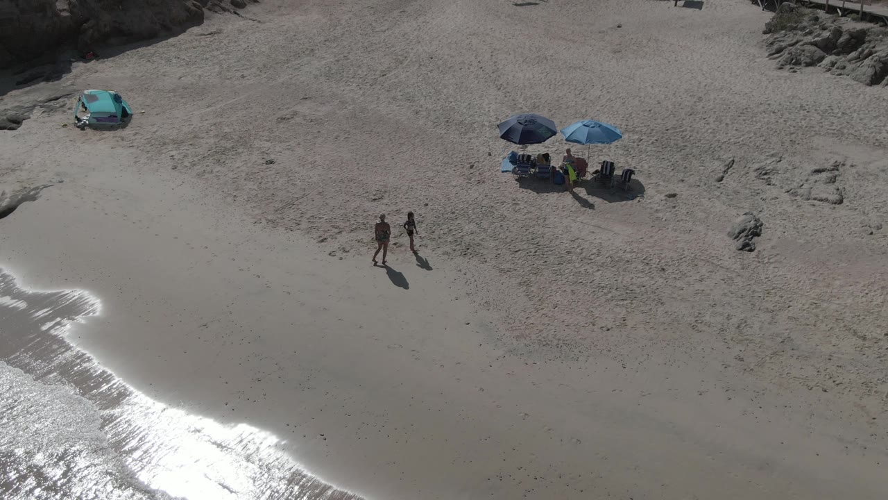 Two beachgoers walking across sand below umbrellas and a turquoise car