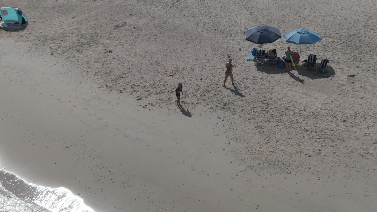 Two people walking on sandy beach near umbrellas and a parked car.