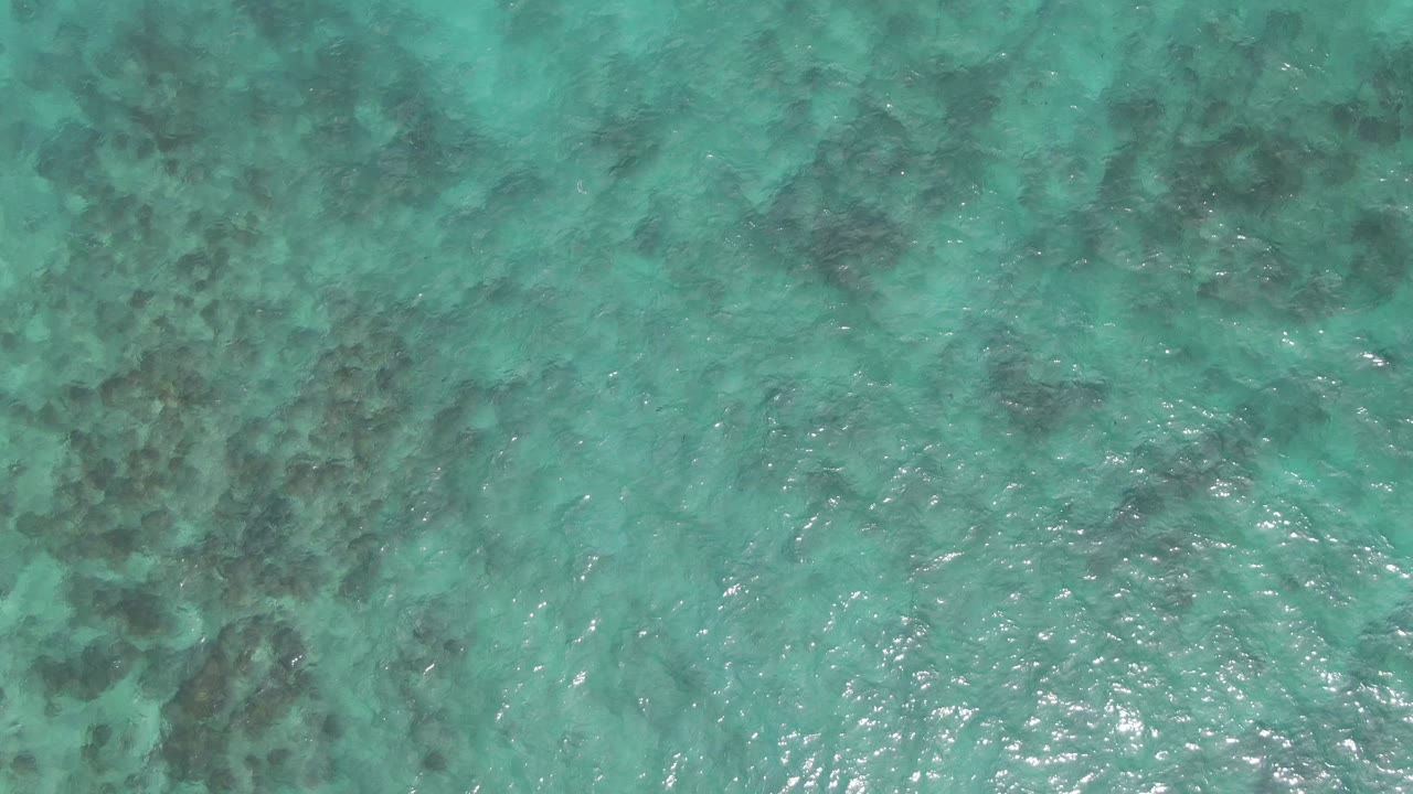 Turquoise sea surface at Playa El Arbolito Cabo Pulmo BCS Mexico, with bright reflected highlights over darker underwater patches and no visible people.