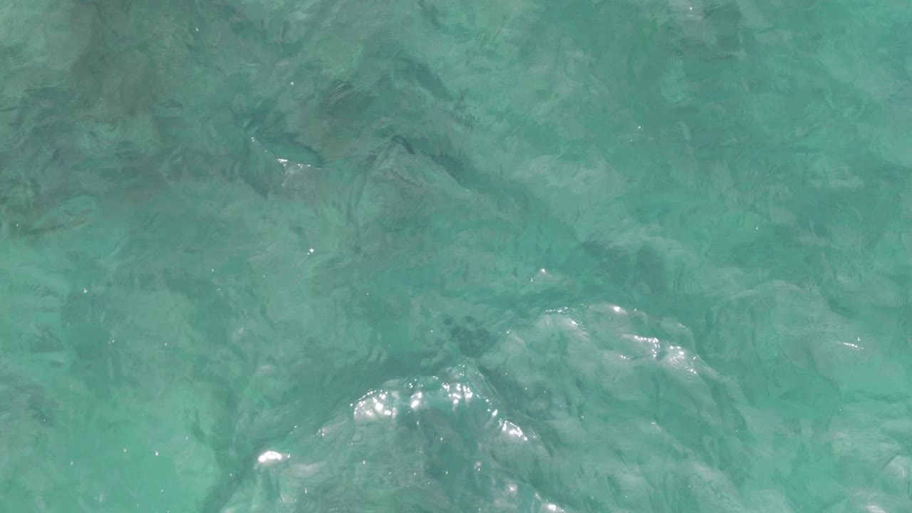 Turquoise shallow sea water at Playa El Arbolito shows brighter reflected highlights near the center, low ripples, visible bottom texture, and no visible people.