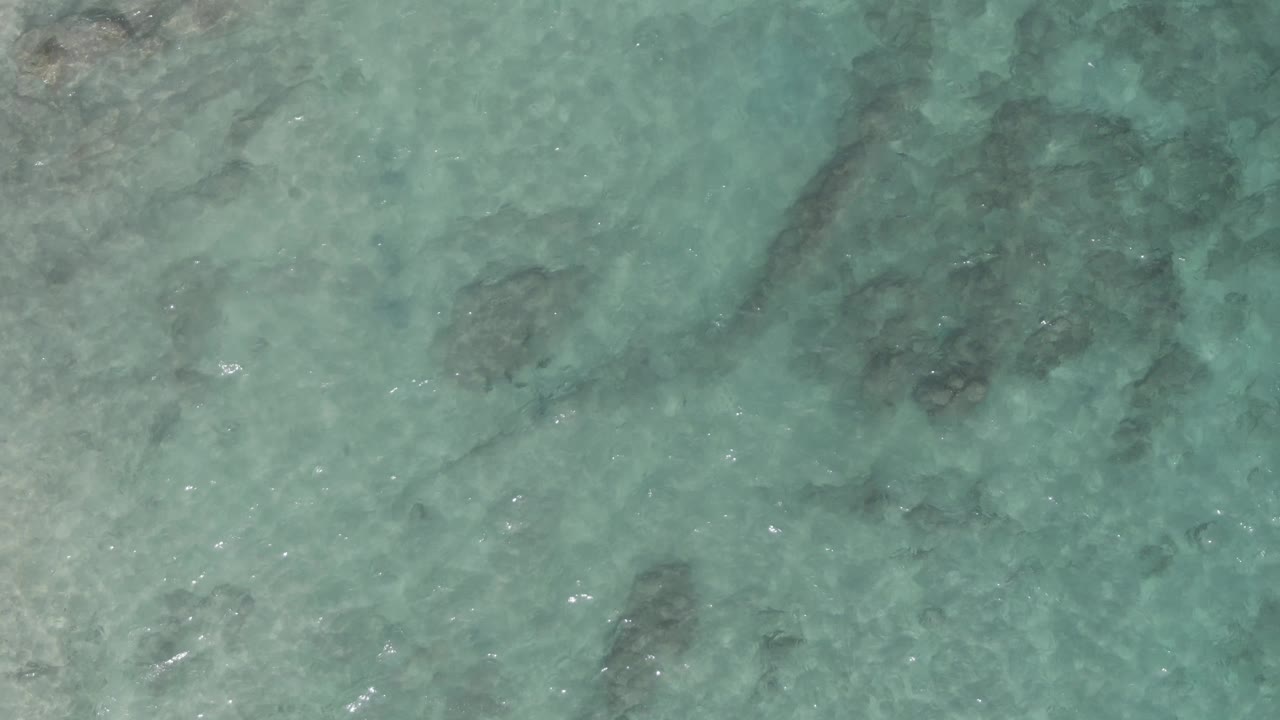 Top-down frame of shallow turquoise water at Playa El Arbolito Cabo Pulmo BCS Mexico, where darker rock patches sit under faint ripples and no visible people appear.