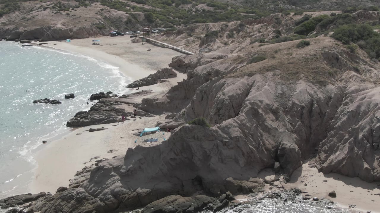 Drone view of waves curving into a beach beside large rock formations.