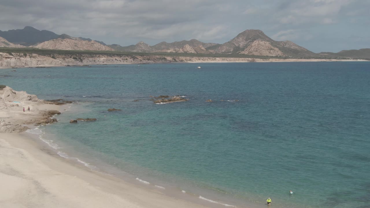 Aerial beach view with people near rocks and swimmers in clear water.