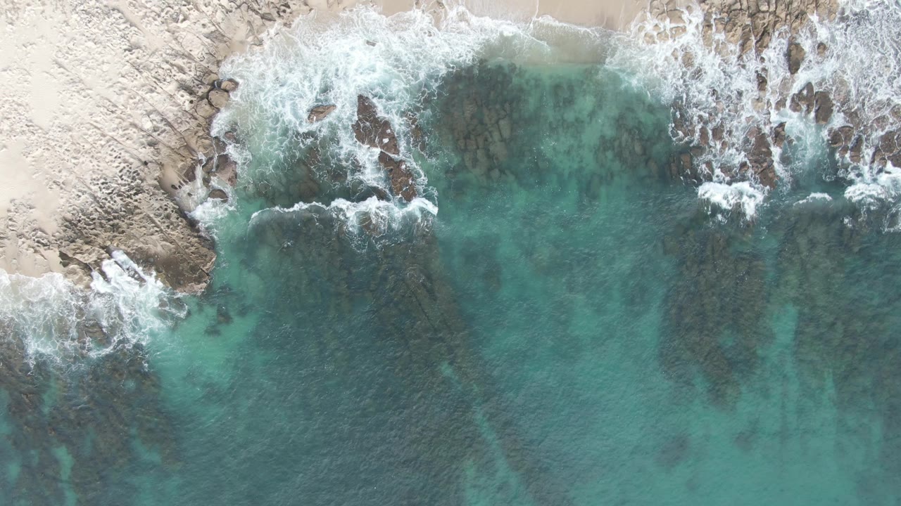 Whitewater spreads around rocks along a sandy shoreline.
