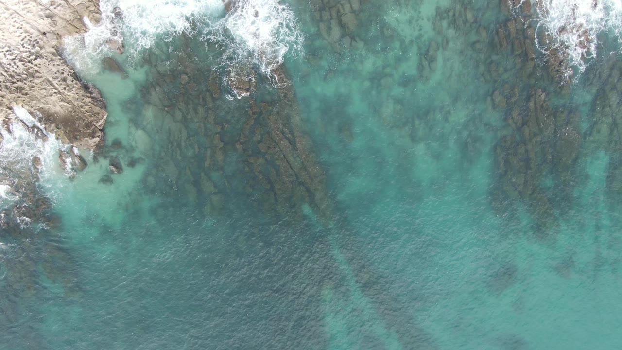 Clear water recedes from a jagged rocky shoreline
