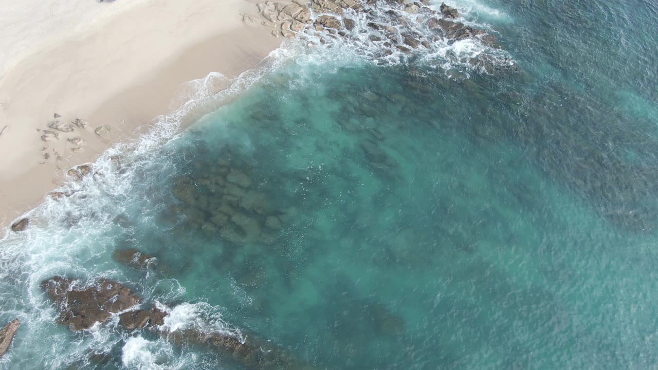 Diagonal shoreline with foamy waves over clear turquoise water