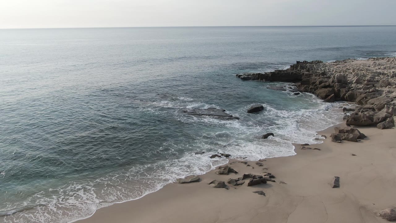 Ocean swell and white wash meet a sandy cove bordered by rocks.